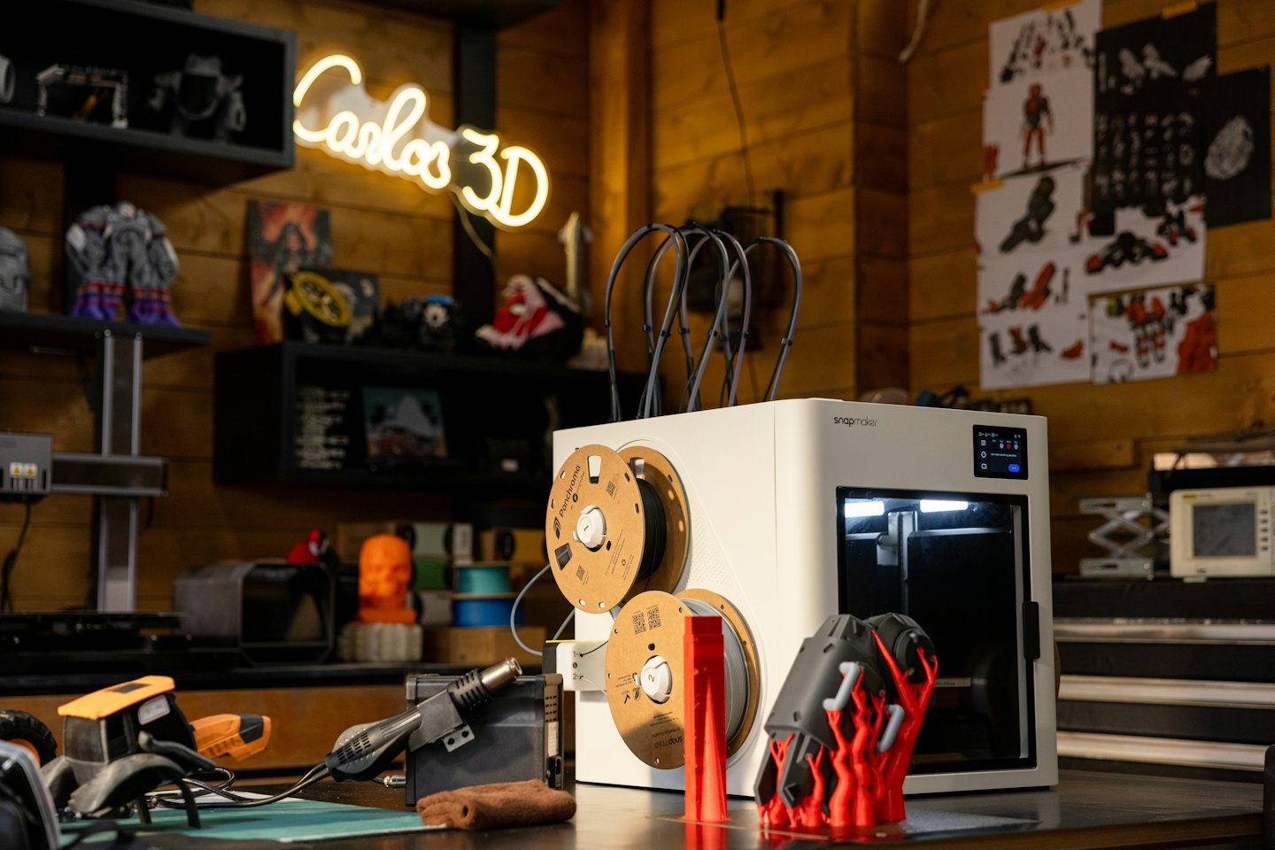 Una impresora 3D moderna crea un objeto rojo sobre un banco de trabajo.